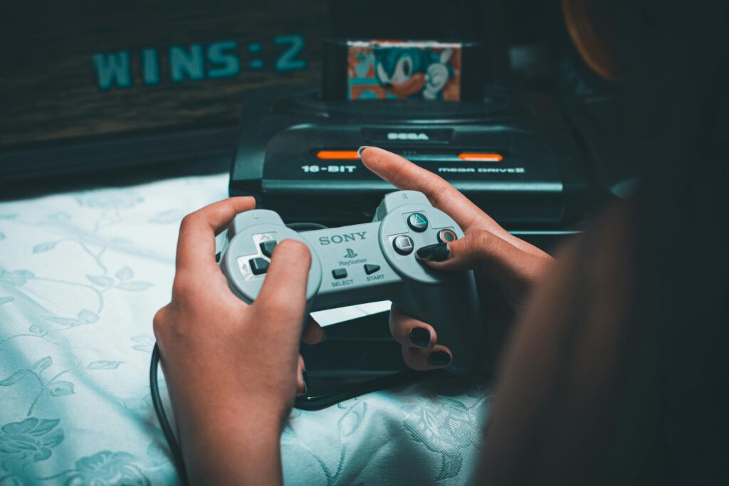 Close-up of hands holding vintage Sony controller with Sega Mega Drive in background.