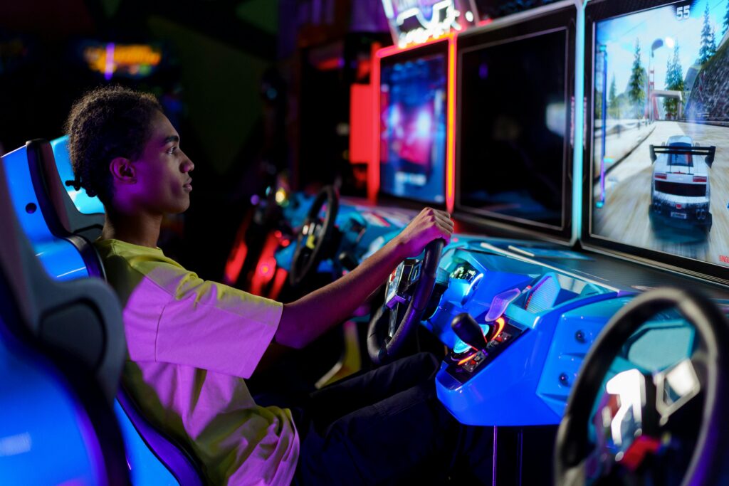 A young man intensely plays a car racing video game at an amusement arcade.